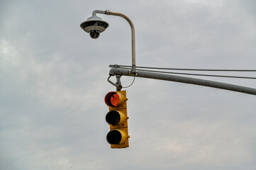 Traffic light with security camera overhead at an urban intersection during overcast weather, signaling red for vehicles