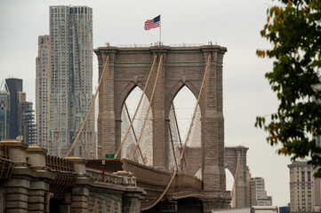 Brooklyn Bridge viewed from below on an overcast day with the American flag waving against a...