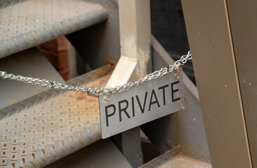 A chain and sign marked private blocking access on a metal staircase in an urban area during daylight hours