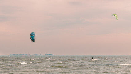 Two kite surfers riding on waves under a pastel sky. Outdoor sports photography at sea.