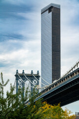 Fototapeta premium A modern skyscraper rises alongside the historic Manhattan Bridge under a dynamic sky in Brooklyn, showcasing the blend of old and new architecture