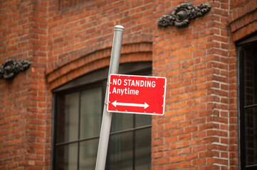 No standing sign in front brick building wall indicating parking regulations in a bustling urban area during daylight hours