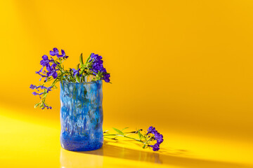 Garden flowers lobelia in a blue glass. Yellow background.