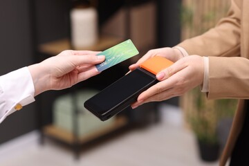 Woman paying with credit card via terminal against blurred background, closeup