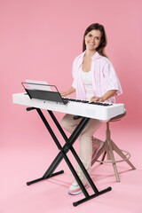 Smiling woman playing synthesizer on pink background