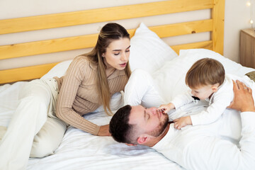 Fototapeta premium Family enjoys playful moment on bed. A couple spends quality time with their young child while relaxing on a cozy bed, creating a joyful family atmosphere.