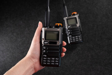 Two professional handheld radios with sleek black designs and antennas placed on a dark textured surface. Compact and durable, these devices are ideal for communication in outdoor or tactical settings © Alisa