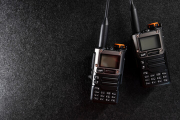 Two professional handheld radios with sleek black designs and antennas placed on a dark textured...