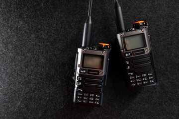 Two professional handheld radios with sleek black designs and antennas placed on a dark textured...