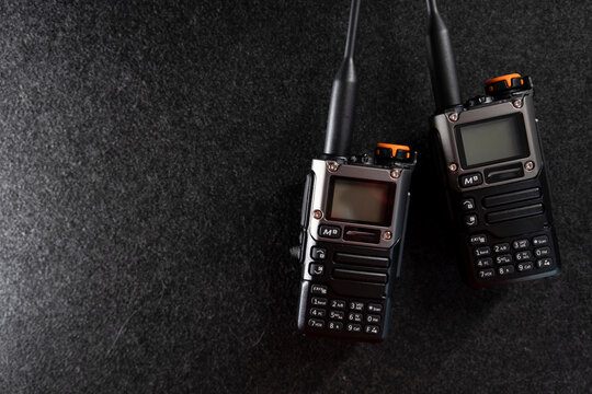 Two professional handheld radios with sleek black designs and antennas placed on a dark textured surface. Compact and durable, these devices are ideal for communication in outdoor or tactical settings