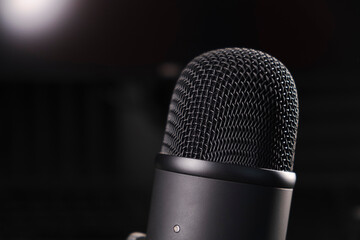 Sleek black microphone on a sturdy stand, placed in a professional recording setup. A modern clock and monitor in the background enhance the studio vibe, perfect for podcasts, streaming, or voiceovers