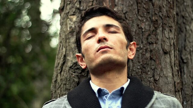 Hopefull man leaning against tree at park