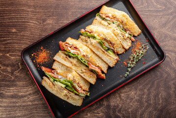 A delicious sandwich cut into pieces, featuring layers of lettuce, tomato, and creamy dressing, arranged neatly on a black tray. Perfect for a tasty lunch or snack.