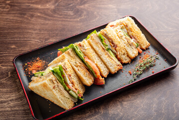 A delicious sandwich cut into pieces, featuring layers of lettuce, tomato, and creamy dressing, arranged neatly on a black tray. Perfect for a tasty lunch or snack.