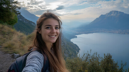 Happy young woman taking a selfie while walking on a mountain with beautiful landscape in the background, enjoying summer vacation