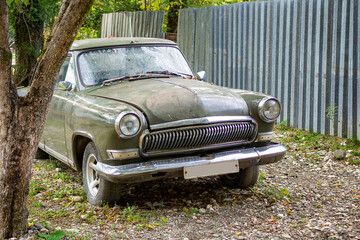 An old green antique car stands by the fence of a holiday home. Foothills of the Caucasus, Abkhazia