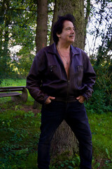 Attraktiver Mann in offener Lederjacke in einem Park.