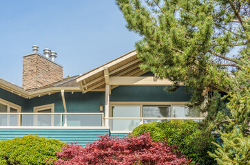 Top of grey stucco luxury house with shingle roof, red and yellow trees and nice windows in Spring in Vancouver, Canada, North America.