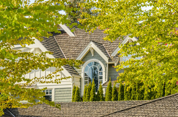Top of grey stucco luxury house with shingle roof, red and yellow trees and nice windows in Spring in Vancouver, Canada, North America.