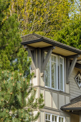 Top of grey stucco luxury house with shingle roof, red and yellow trees and nice windows in Spring in Vancouver, Canada, North America.