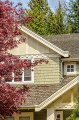 Top of grey stucco luxury house with shingle roof, red and yellow trees and nice windows in Spring in Vancouver, Canada, North America.