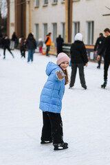 Beautiful happy girl child teenager skating on ice on outdoor rink waving hand. Photography, portrait, hobby and sport concept.