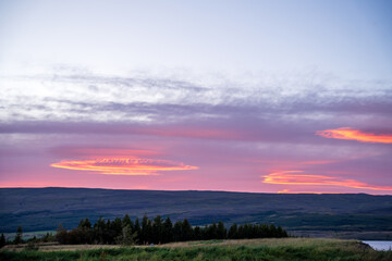 Obraz premium The tranquil waters of Lake Lögurinn reflect the warm hues of a glowing sunset, framed by an unusual cloud pattern in east Iceland