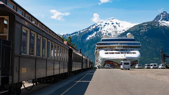 Skagway, Alaska, USA - July 07, 2019: Norwegian Jewel. White Pass and Yukon Railway train. Railway train and cruise ship. Train railway station. Scenic Yukon ride landscape in Alaska. Scenic