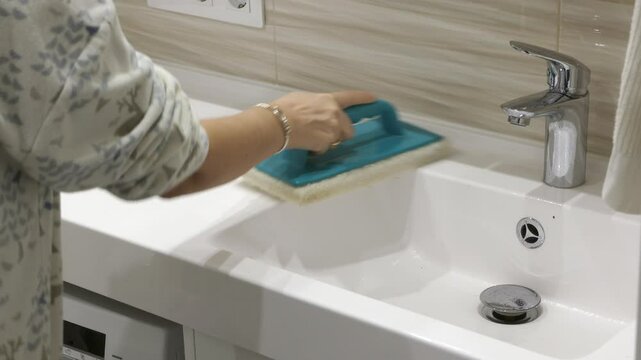 Woman cleaning bathroom. Female hands with handheld pad holder cleaning white sink in bathroom.