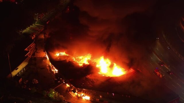 Aerial view of a large building fire threatening a busy road, during night-time