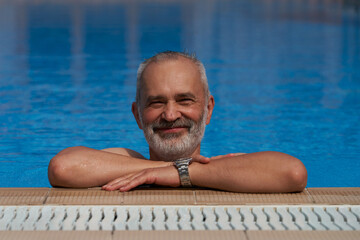Smiling adult male in water droplets at the edge of an azure water swimming pool.