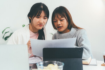 Female higher education student using laptop and studying book in home, Online learning.