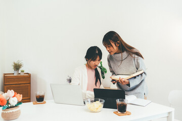 Female higher education student using laptop and studying book in home, Online learning.