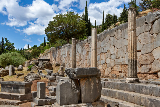 Ancient ruins of the Temple of Apollo in Delphi, Greece, showcasing preserved stone columns and a polygonal wall with a scenic mountainous backdrop.