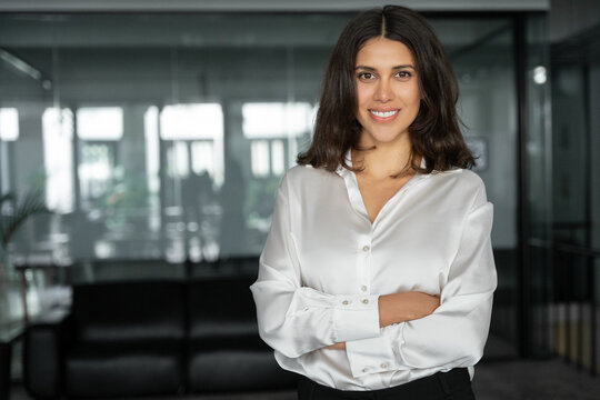 Smiling latin hispanic business woman employee with crossed arms looking at camera. European or eastern confident good looking middle age female leader businesswoman standing in office. Copy space.