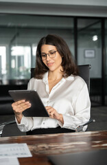 Middle eastern businesswoman holding digital tablet using tab application sitting at desk workplace...