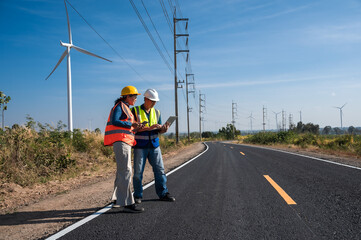 Male Japanese wind turbine engineer working with laptop computer in wind power plant with female electrician coworker 