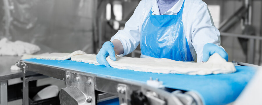 Food industry worker technologist prepares puff pastry dough on automated conveyor in confectionery production