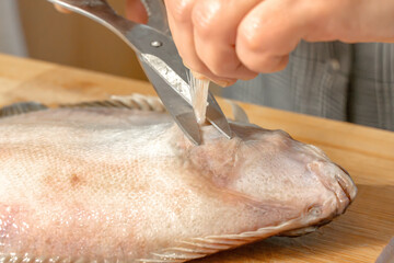 Chef uses scissors to cut out a fin from a fresh flounder