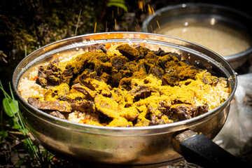 A rustic outdoor dish featuring mushrooms, aromatic curry spices, and brown rice in a metal pan, perfect for themes of healthy eating, nature, and camping.