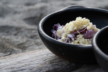 black bowl containing finely chopped garlic and red cabbage, placed on a wooden surface against a natural outdoor background. The scene evokes rustic cooking and natural ingredients