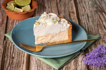 Torta de limão com creme de merengue de cobertura em um prato de ceramica azul sob uma mesa de madeira com um potinho de limões cortados, planta de lavanda e pano ao redor  