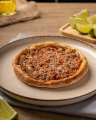 esfiha de carne em um prato de ceramica sob uma mesa de madeira e elementos ao redor como limão, azeite e um pano