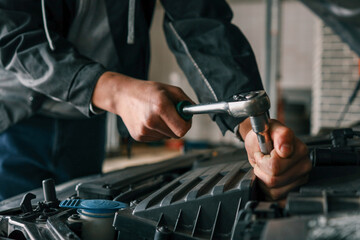 Mechanic tightening a bolt on a car engine using a ratchet wrench in a professional workshop setting
