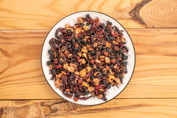 Carpathian forest tea in a white ceramic saucer on a wooden table, macro, top view.