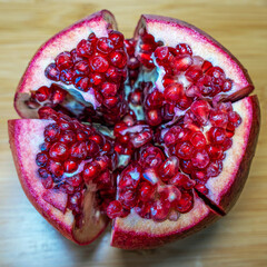 Top view of a fresh ripe pomegranate fruit cut into beautiful slices, square photo.
