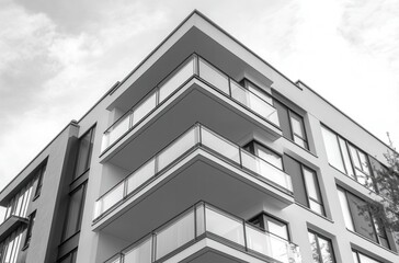 Obraz premium Modern architectural design of a residential building featuring sleek lines, large windows, and spacious balconies in a monochromatic aesthetic against a cloudy sky.