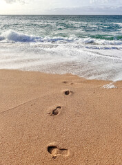 A picturesque vertical view of footprints in the golden sand of a pristine Maldives beach, surrounded by turquoise waters.