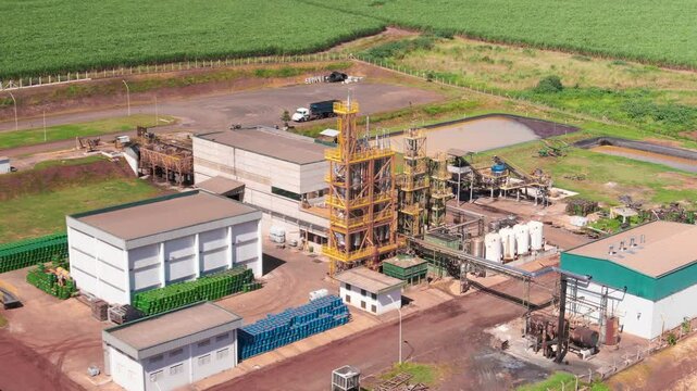 Aerial pull back shot of small refinery located at countryside during daytime.
