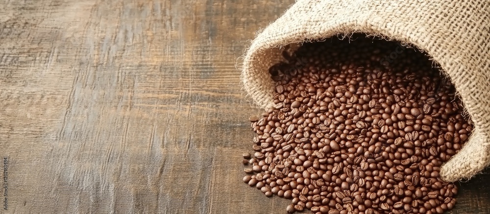 Poster brown coffee beans spilling out of a burlap sack on a wooden surface with copy space for text